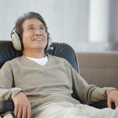 Mature man leans back in armchair, wearing headphones, smiling