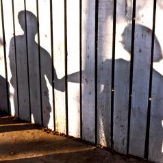 White painted fence displays shadow of teen boy taking adult