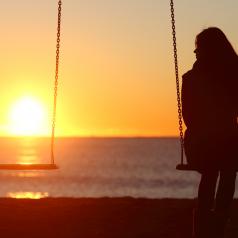 Girl looking at empty swing at sunset