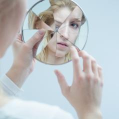 Person with long blonde hair looks into broken hand mirror to piece together reflection