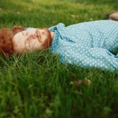 Young adult with red hair and beard, wearing light blue buttondown shirt, lies on grass with eyes closed