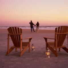 Rear view of couple on shoreline at dawn. Foreground of picture centers on beach chairs and lanterns close together