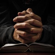 Hands clasped in prayer and resting on book