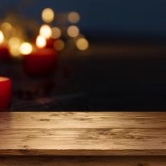 Single red candle burns on empty wooden table, blurred lights in dark background