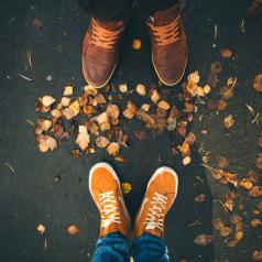 View of the feet in outdoor shoes of two people on ground with leaves. The feet are facing but standing apart