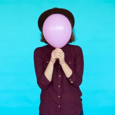 holding balloon over face in front of turquoise background