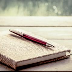 Pen lies on notebook on wooden table with rainy weather visible outside window