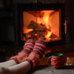 Legs in socks rest in front of fireplace in dark room, with a red and green mug nearby