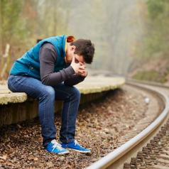 Fall scene of young adult with head in hands sits on ledge next to curving train track