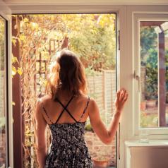 Rear view of person with long hair in tank top standing in open doorway and looking outside
