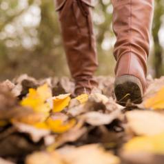 Close-up photo of booted feet walking through leaves