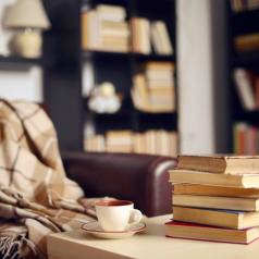 Focus is on corner with soft blanket, tea, and books. Two tall bookcases in blurred background