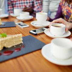 Focus on cake and tea at restaurant table, cropped view of several friends with smartphones on table