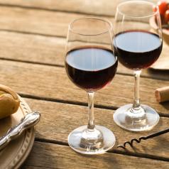 Two half-filled glasses of red wine on picnic table with bread and cheese in the afternoon