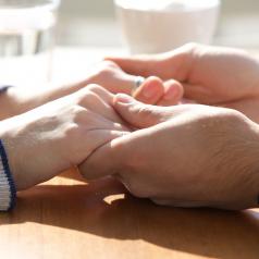 Close-up shot of two people holding hands on top of a table, water glasses out of focus in background