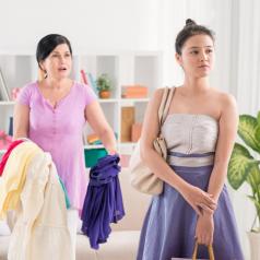 Parent holds out clothes and attempts to converse with teenager looks away and off to the side 