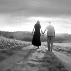 Black and white photo of couple walking into distance along trail holding hands 