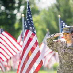 Military woman saluting in front of flags