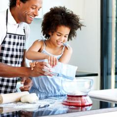 Father and child of 6-8 years wear aprons and prepare a meal in the kitchen together smiling