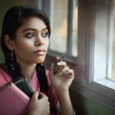 Close-up image of young adult with two braids looking out window with worried, thoughtful expression