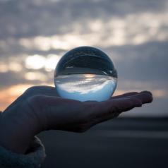 Image of a hand holding a glass globe with reflections of a sunset inside it.