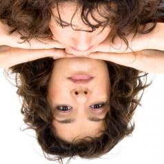 Person with curly long hair looks down into mirrored table. Reflection looking up is somewhat distressed
