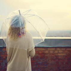 Woman under umbrella looking out over brick wall