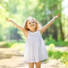 Young child with long blonde hair stretches arms up happily