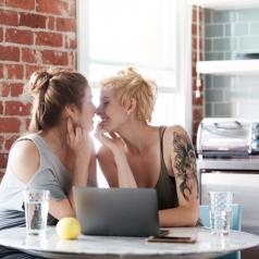 Happy couple looks at each other, leaning in close to kiss in front of open laptop