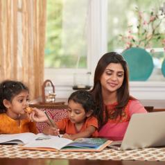 Cheerful but busy mother works on laptop while taking care of two children