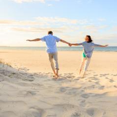 Rear view distance photo of couple holding hands leaning apart while running through sand on beach
