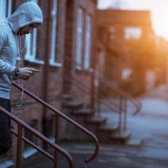 Young adult in light gray hoodie heads down steps holding music player to go on run