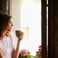 Shot of a young woman drinking a cup of coffee while looking out of a window