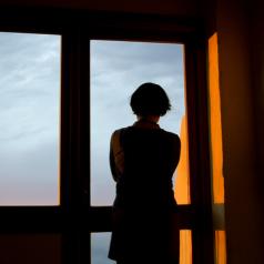 Person in shadow looking out high window into cloudy sky