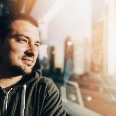 Adult with close-cropped dark hair looks out train window in contemplation while traveling through city
