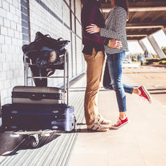Young couple excited to start trip embraces and kisses on tiptoe outside city