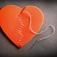 A broken heart with a needle and thread stitching it back together.