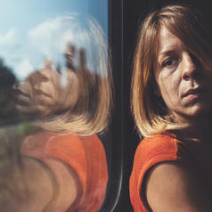 Side view of person with shoulder-length hair looking to the side out window of train