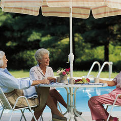 Three mature adults with short hair sit at decorated table by pool enjoying coffee