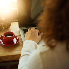 Rear view of person with curly hair using laptop next to coffee cup