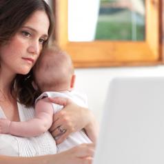 Mother holding baby while looking at computer
