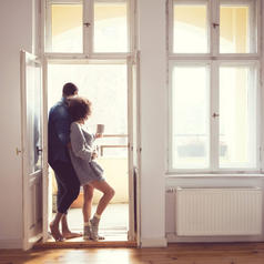Couple leans into each other in front of open door by walls of windows in bright house