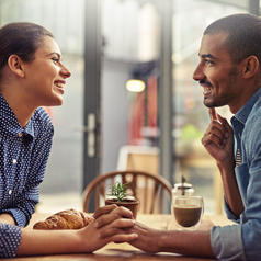 Shot of a young couple enjoying their date at a local coffee shop talking holding hands
