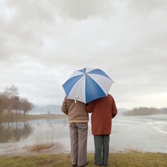 Senior couple under an umbrella in the rain by a lake.