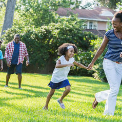 Family with two children run playfully together across suburban lawn