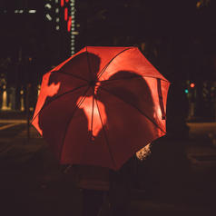 Silhouettes of couple about to kiss are visible behind a red umbrella