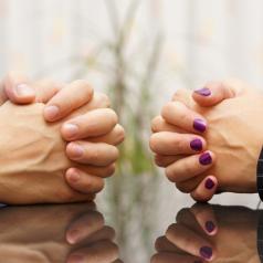 Cropped image of folded hands of two partners seated at opposite sides of table
