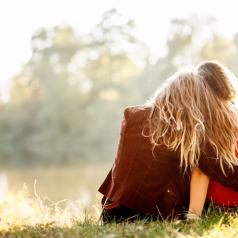 Rear view of two young adults with long hair sitting on grass. one hugs the other
