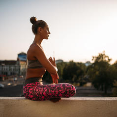 Person seated in yoga pose on ledge wearing athletic clothes, hair in bun