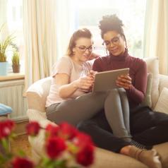 Couple sits together with legs crossed together using tablet and smiling